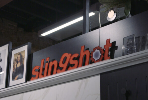 A mantlepiece with framed photos and a sign that says Slingshot.